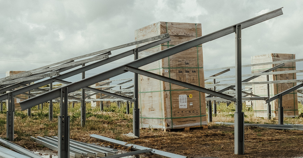 An image of solar panels facing skyward with pallets of materials stood between them.
